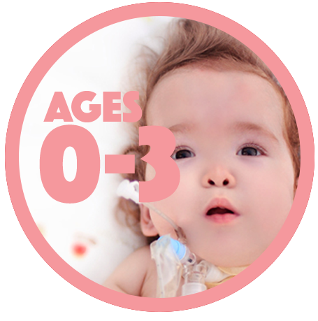 Infant with Down syndrome lying on a white blanket with red and yellow dots. Infant has a feeding tube.