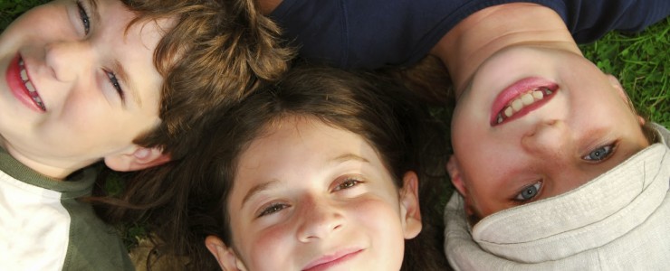 three children lying on the ground, looking up, smiling