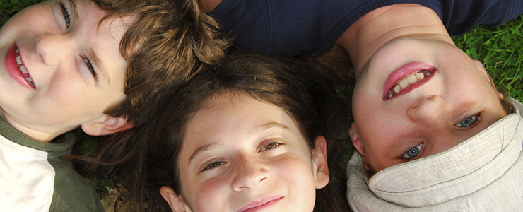 Portrait of three young children lying on grass looking up