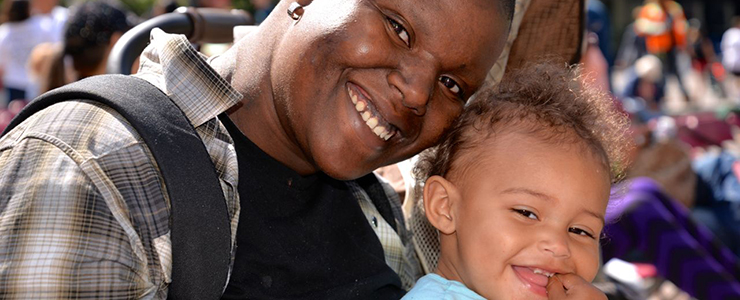 Smiling parent and toddler at an outdoor event.
