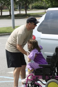 father lifting daughter out of her wheelchair, into van