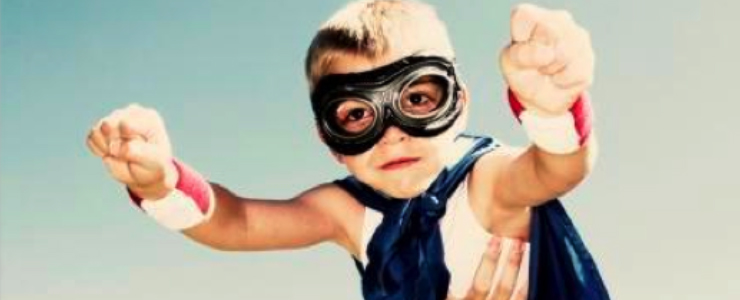 child in goggles and cape being held in the air to fly