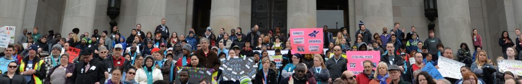 Front of Legislative Building in Olympia. Crowd of disability advocates waving signs on the front steps.