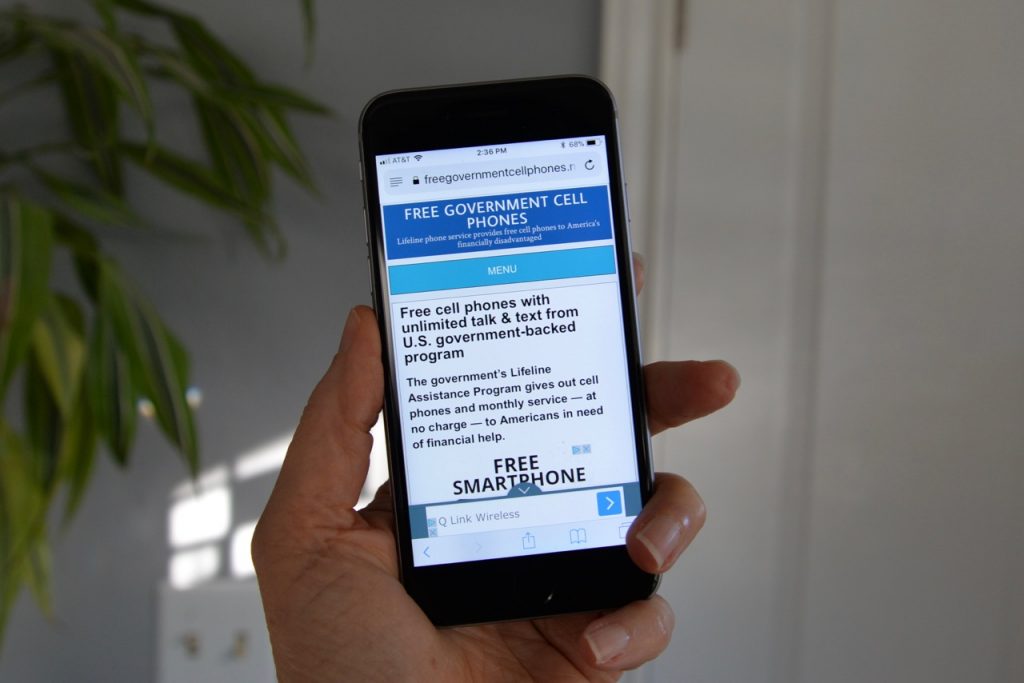 hand holding a cell phone with freegovernmentcellphones.net homepage displayed on the screen.
