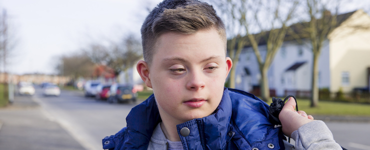 A young man with Down syndrome carries a bag as he walks along a street.