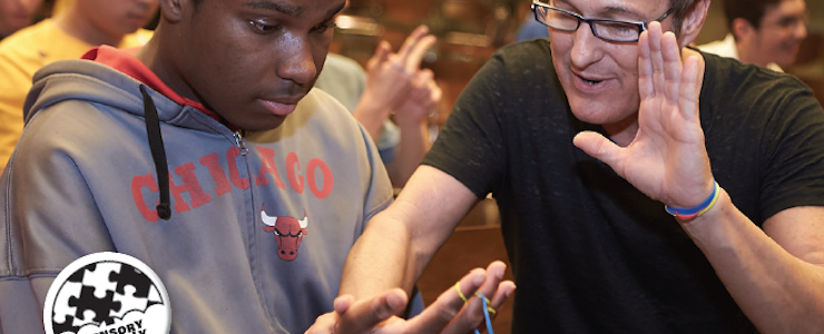 Magician instructs a young man with disabilities how to perform a magix trick.