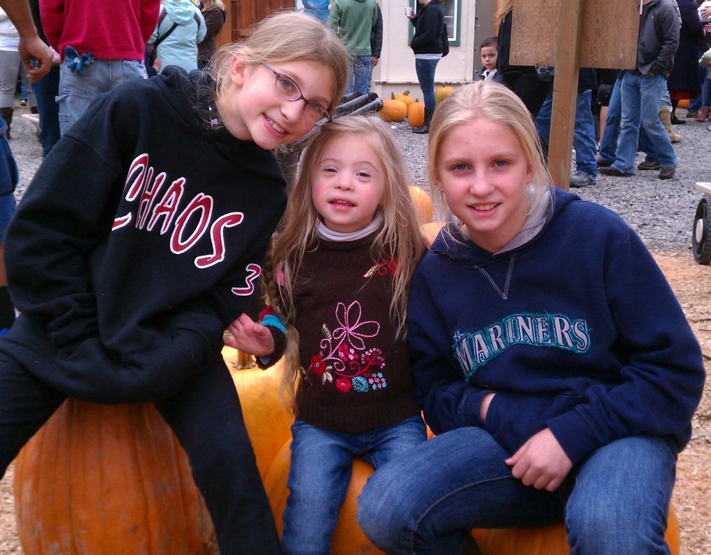 Three sisters sitting on giant pumpkins.