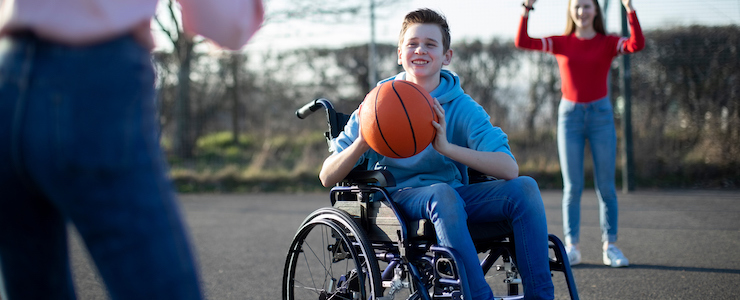 Teenage Boy In Wheelchair Playing Basketball With Friends