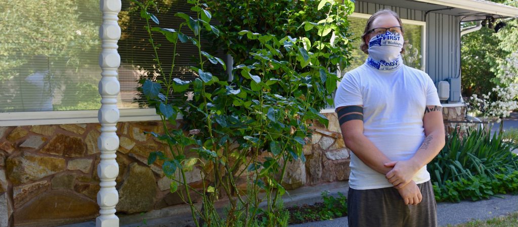 Man wearing People First gaiter, standing in front of house.