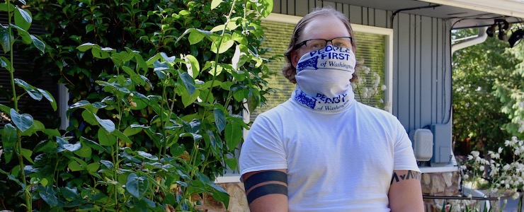 Man wearing People First gaiter, standing in front of house.