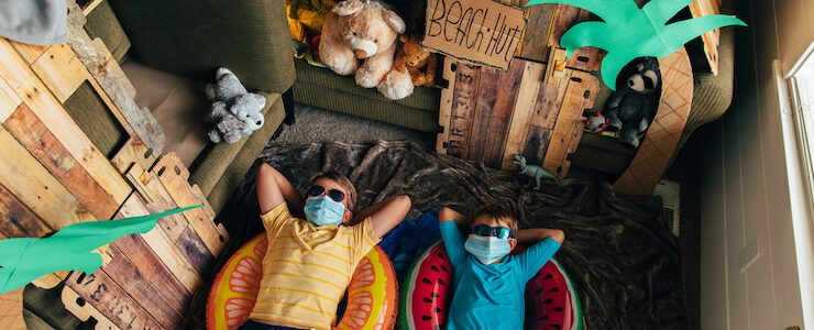 Two youth wearing masks, lying in their living room decorated as summer camp.