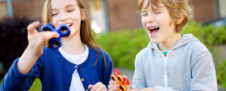 Two funny friends playing with colorful fidget spinners on the playground. Popular stress-relieving toy for school kids and adults.